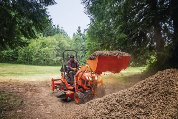 Man using sub compact tractor to move dirt onto pile.