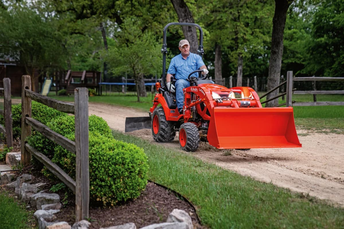Man using box blade implement on a dirt driveway