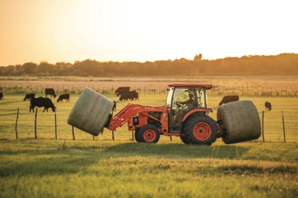 Tractor moving two hay bales with front and rear attachments