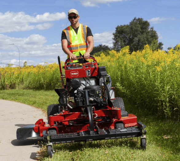 Man mowing an overgrown area with a stand-on mower
