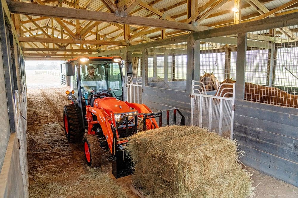 Tractor moving hay into stalls for horses