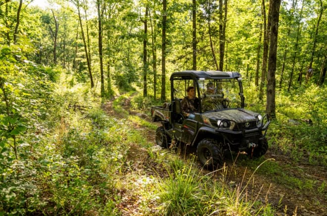 Kubota Sidekick utility vehicle in camouflage driving down a wooded trail