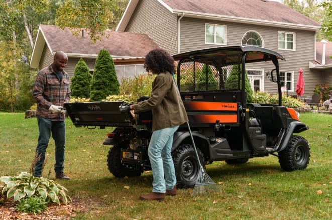 Kubota RTV-X diesel utility vehicle with couple loading yard debris into cargo bed at a residential home
